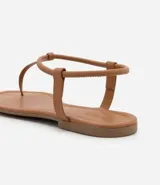 Sandalia plana de mujer color dorado metalizado, con diseño minimalista de tira fina que une la puntera y el empeine, y tira elástica fina alrededor del tobillo.