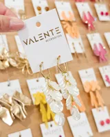 Aros colgantes compuestos por una argolla de acero dorada y un dije formado por múltiples pétalos de resina en color blanco perlado.