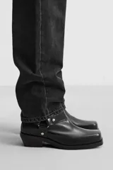 Bota corta negra de cuero con horma cuadrada, tacón bajo y arnés decorativo con remaches plateados a la altura del tobillo.