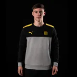 Buzo de cuello redondo Puma del Club Atlético Peñarol. Presenta un diseño de bloques de color con la parte superior y mangas en negro, franjas amarillas en los hombros y el cuerpo central en gris melange. Incluye el logo de Puma en amarillo y el escudo del club en el pecho.