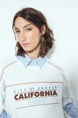 Remera negra de manga corta con estampado tipográfico "City of Angels California 1997" en tonos marrones y costuras visibles en blanco.