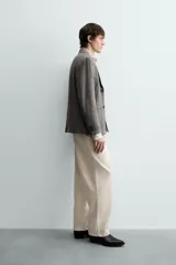 Pantalón chino de corte relajado, confeccionado en tejido estructurado de color beige. Presenta bolsillos frontales, bolsillos traseros de vivo y cierre frontal con cremallera y botón.