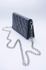 Bandolera negra de cuero sintético con diseño capitoneado y cadena metálica plateada. Interior forrado en tela roja con ranuras para tarjetas.