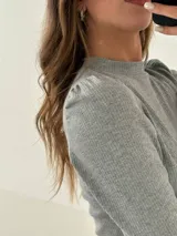 Remera de manga larga confeccionada en tejido morley de algodón, con cuello redondo y detalle fruncido en los hombros.