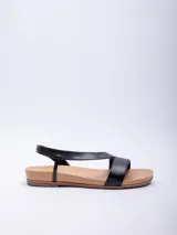 Sandalia baja de mujer, color negro, con doble cinta cruzada sobre el empeine y tira elástica para ajuste en el tobillo. La base es de color marrón claro.