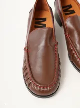 Mocasines de cuero negro con costuras pespunteadas en hilo blanco a contraste, diseño fruncido en la puntera, talón plano con pequeño tacón y apliques sutiles en charol.