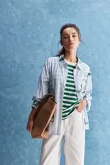 Camisa de calce relajado con cuello clásico, mangas largas con puños elastizados y rayas verticales que aportan un estilo atemporal. Su diseño liviano y versátil cuenta con estampado floral verde sobre fondo de rayas celestes y blancas.