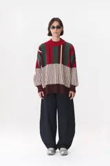Buzo oversize de tejido de punto con diseño de bloques y rayas verticales en colores rojo, verde, bordó y crema. Presenta cuello alto tejido y terminaciones en rib en puños y ruedo.
