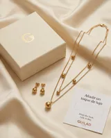 Set compuesto por un collar doble de cadena fina con dijes de esferas doradas y un par de aros tipo caravana con dije de esfera dorada, confeccionados en acero con baño de oro.