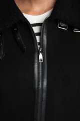 Campera tipo gamulán de corte oversize, color negro, con interior y detalles en cuello y puños de corderito sintético. Presenta cierre frontal y correas decorativas en el cuello.