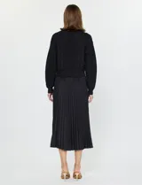 Conjunto compuesto por un buzo de tejido calado con cuello redondo y mangas largas, y un vestido midi de satén con falda plisada. Ambas piezas son de color negro y pueden combinarse o utilizarse por separado.