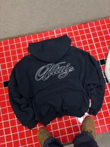 Hoodie negro con capucha y estampa gráfica blanca en la espalda con diseño tipográfico cursivo. Presenta puños y ruedo acanalados.