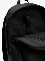 Mochila urbana de diseño minimalista confeccionada en poliuretano negro. Presenta un compartimento principal amplio con cierre, un bolsillo frontal con textura acanalada y el logo de la bandera de la marca en la esquina inferior. Incluye correas de hombro acolchadas y ajustables, además de un asa superior de mano.