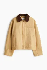 Campera de algodón Oxford color beige con cuello de pana marrón en contraste. Presenta un diseño de corte holgado con hombros caídos, cierre frontal de cremallera, bolsillos laterales ribeteados y un bolsillo superior con cierre. Incluye puños y bajo ajustables con botones a presión.