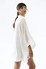 Camisa de lino blanca con corte oversize, cuello camisero y mangas amplias tipo kimono. Presenta detalles de costuras decorativas en el frente y cierre frontal con botones.