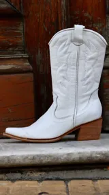 Bota texana blanca de caña media realizada en cuero engrasado, con detalle de punta fina y bordado decorativo. El interior está forrado en cuero vacuno. El taco es de madera.