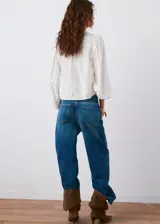 Blusa blanca de algodón con bordados florales, cuello alto con volados y mangas largas abullonadas con puños ajustados.