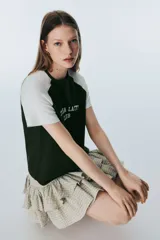 Remera de manga raglán con cuerpo en color verde oscuro y mangas en color blanco. Presenta cuello redondo y estampado frontal con la inscripción 'MATCHA LATTE CLUB' en tipografía universitaria.