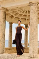 Vestido largo color chocolate con tirantes finos, escote recto y detalle de nudo en la cintura que crea una abertura en la falda.