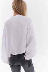 Camisa blanca de lino italiano, de corte holgado, mangas largas abullonadas, cuello mao y cierre frontal con botones, con diseño para anudar en la cintura.