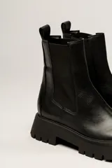 Bota Chelsea color verde militar de cuero, con elásticos laterales negros, tirador trasero y suela track negra.