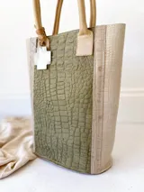 Bolso matero verde con textura croco y detalles en beige. Tiene doble asa corta y accesorio metálico en forma de cruz.
