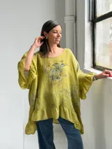 Blusa color verde pistacho, de corte holgado, manga corta con volados y diseño asimétrico con volado en el ruedo. Cuenta con un estampado floral difuminado en el frente.