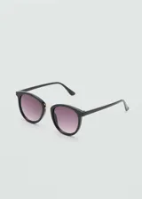 Gafas de sol con montura redonda de pasta color negro, puente metálico dorado y cristales degradados en tono rosado.