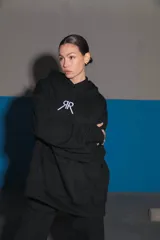 Buzo negro oversize de frisa con capucha amplia, bolsillo canguro, terminaciones de puño y ruedo con rib, y logo bordado en el centro delantero.