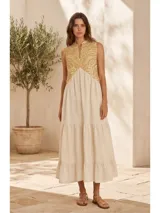 Vestido largo sin mangas, color blanco marfil con detalles bordados en tono dorado en la parte superior, escote en V y diseño de falda con volantes escalonados.