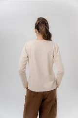 Remera manga larga color beige melange, confeccionada en algodón con spandex, con escote redondo y cartera delantera con botones y detalle de cordón tejido multicolor.