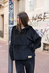 Canguro unisex negro de tela suave con capucha y bolsillo delantero tipo canguro. Tiene cordón ajustable en la cintura para usarlo largo o corto.