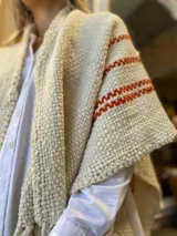 Ruana color crema tejida en lana merino con rayas horizontales color ladrillo y flecos largos en el ruedo.