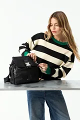 Bandolera de nylon color negro con tapa frontal y cierre de hebilla metálica. Cuenta con correa regulable, bolsillos laterales con cierre y compartimento principal con cierre.