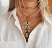 Collar con gargantilla doble de cuero color naranja y dije colgante con forma de hoja color bronce y tres piedras verdes. El dije tiene textura martillada.