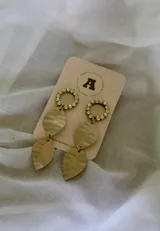 Aros colgantes dorados con círculos de strass y dijes de hojas texturizadas.