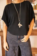 Blusa negra de corte holgado con mangas cortas tipo murciélago y cuello redondo. Confeccionada en tela con textura sutil.