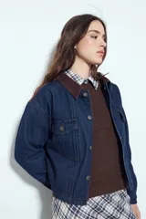 Campera de jean color negro con cuello de pana en tono marrón, cierre frontal con botones y bolsillos en el pecho. Presenta un diseño de corte relajado y ligeramente cropped, con interior forrado en corderito para mayor abrigo.