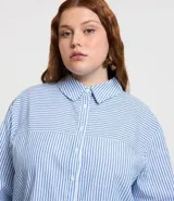 Camisa plus size alargada confeccionada en tela anarruga a rayas verticales celestes y blancas, con cuello inglés, botones delanteros para cierre y mangas largas con puños abotonados.