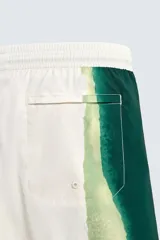 Bañador de hombre color blanco con diseño de bandas verticales en tonos de verde, simulando un efecto tie-dye o acuarela. Posee cintura ajustable con cordón, bolsillos laterales y forro interior.