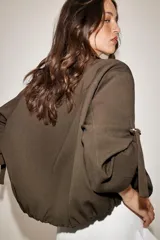 Chaqueta bomber color marrón, con cuello solapa, cierre frontal oculto con cremallera y botones a presión. Presenta mangas remangadas con trabillas y bajo abullonado con elástico interior.