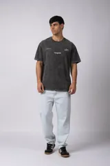 Remera de algodón con efecto lavado gastado, cuello redondo y mangas cortas. Presenta estampados minimalistas en el frente con el logo de la marca y la frase 'Local Based, Global Attitude'.