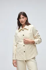 Camisa de lana fina sin teñir, color marrón, con diseño capitoneado y pespuntes decorativos. Presenta cuello clásico, cierre frontal con botones metálicos y dos bolsillos frontales tipo parche.