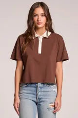 Remera de manga corta color marrón con cuello polo y solapa frontal con botones en color blanco contrastante, de corte recto y holgado.