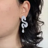 Par de aros colgantes negros con forma de S alargada y dije en forma de gota.