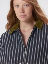 Campera de denim a rayas verticales con cuello de pana en color bordó. Presenta cierre frontal, mangas desmontables con cierre en los hombros, canesú en el pecho y bolsillos de parche cuadrados.