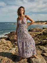 Vestido largo con escote halter profundo, cintura marcada y falda amplia con volados, en color crema con estampado multicolor de inspiración paisley y floral en tonos azules y rojizos.