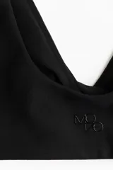 Top de yoga negro confeccionado en tejido funcional con tecnología SoftMove y Lycra Sport. Presenta un diseño con breteles anchos, escote en V y un detalle cruzado o girado en la parte delantera. Incluye copas con relleno extraíble y ofrece sujeción suave para ejercicios de bajo impacto.