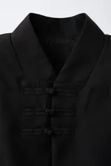 Capa de estilo oriental en color negro, con cuello mao, cierre frontal de alamares y mangas anchas. Presenta un estampado gráfico tonal en toda la prenda y un cinturón de cuerda trenzada ajustable en la cintura.