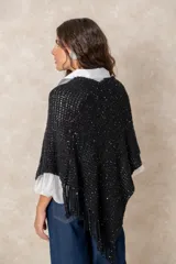 Poncho negro de tejido calado con destellos brillantes y terminación de flecos en el ruedo.